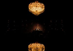 Two elegant crystal chandeliers illuminating a dark auditorium space during an evening event.