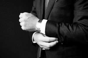 Close-up black and white photo of hands adjusting suit cuffs and watch.