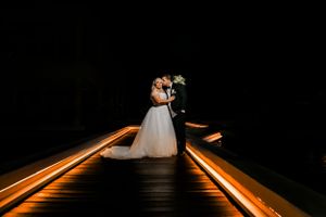 Dramatic nighttime portrait of newlyweds on an illuminated boardwalk with light trails.