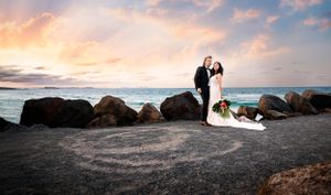 Sunset wedding photo of couple silhouetted against ocean and rocky shore.
