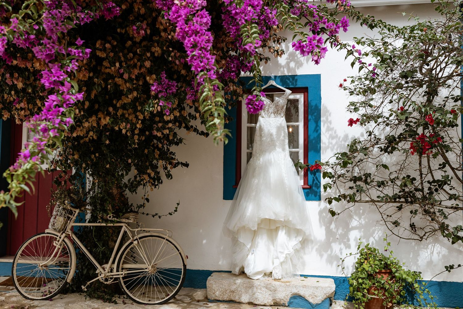 A wedding dress hangs on a white wall with pink bougainvillea at Quinta da Bichinha