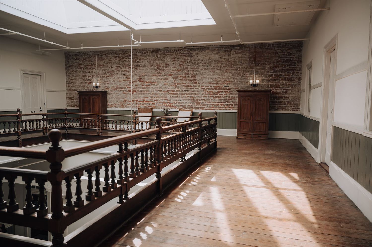 Historic building interior with wooden railings, exposed brick walls and hardwood floors illuminated by natural light.