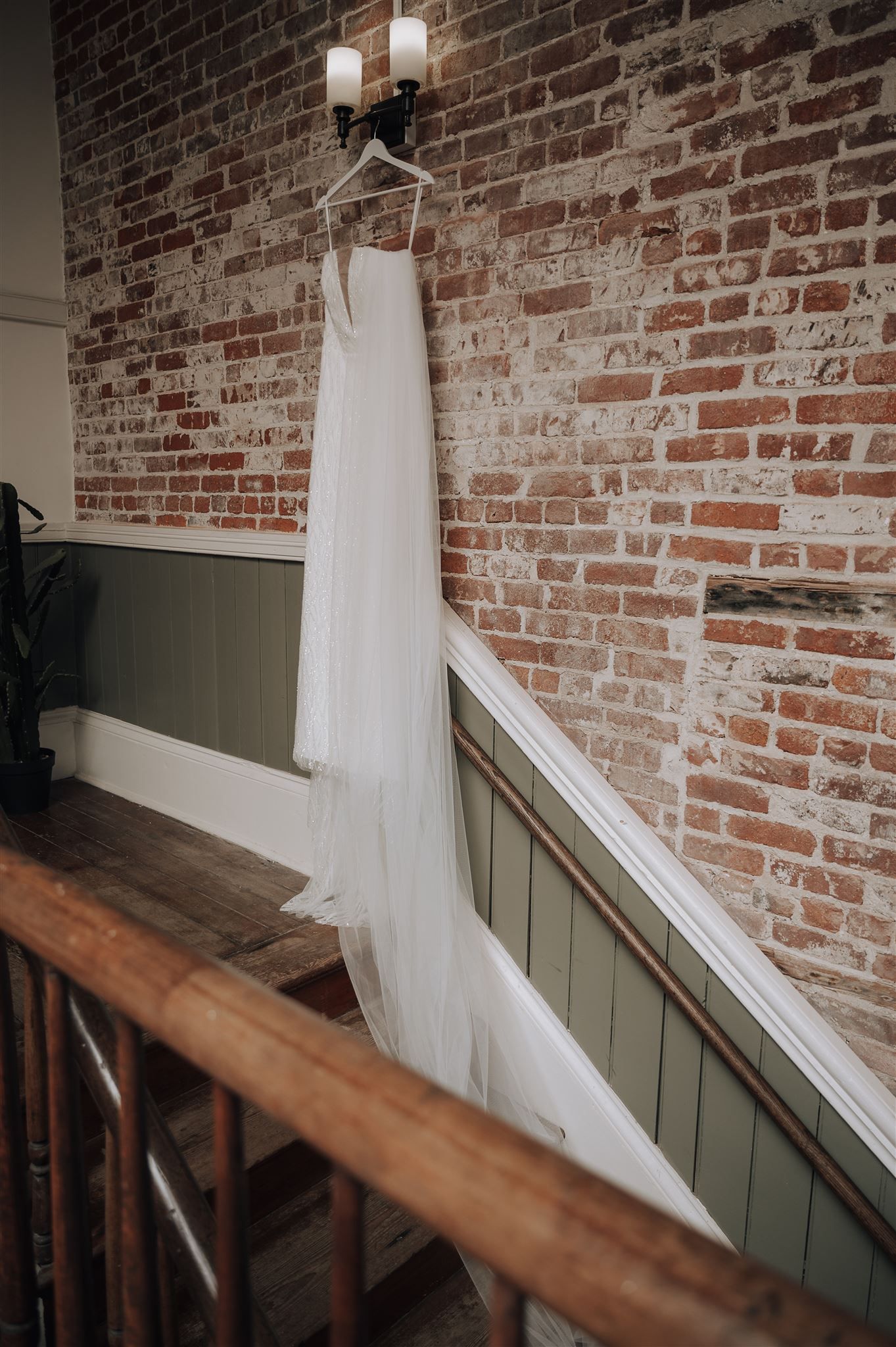 White wedding dress hanging on wall with exposed brick and wainscoting.