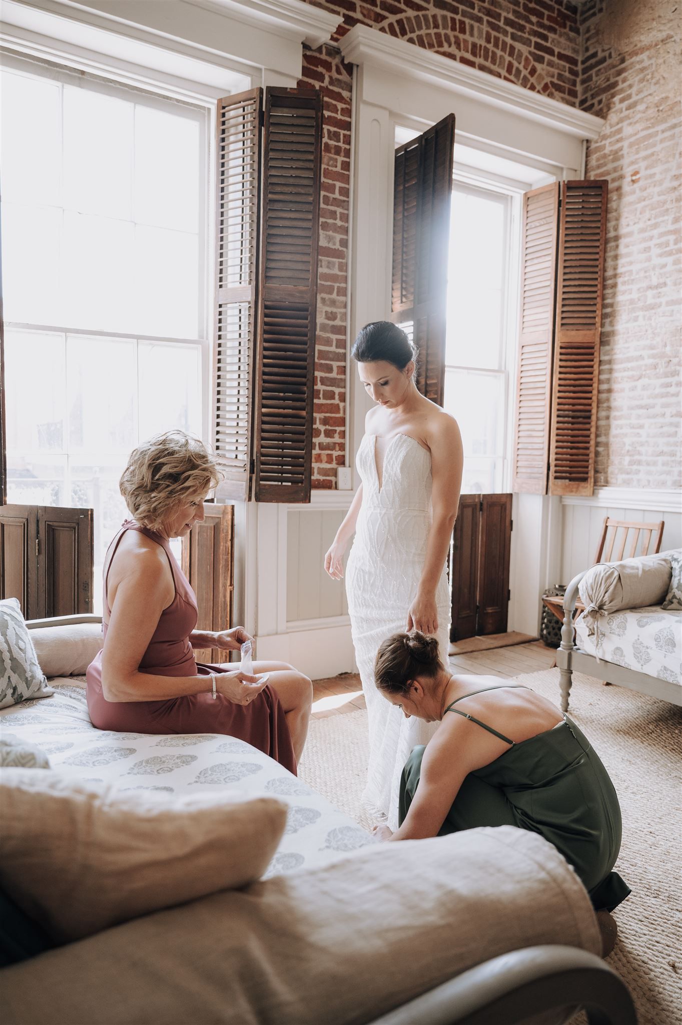 Wedding dress fitting in a rustic brick room with tall windows.