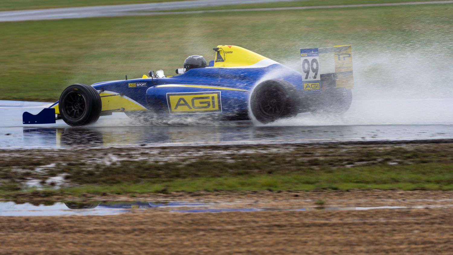 Formula racing car spraying water while driving on wet race track.