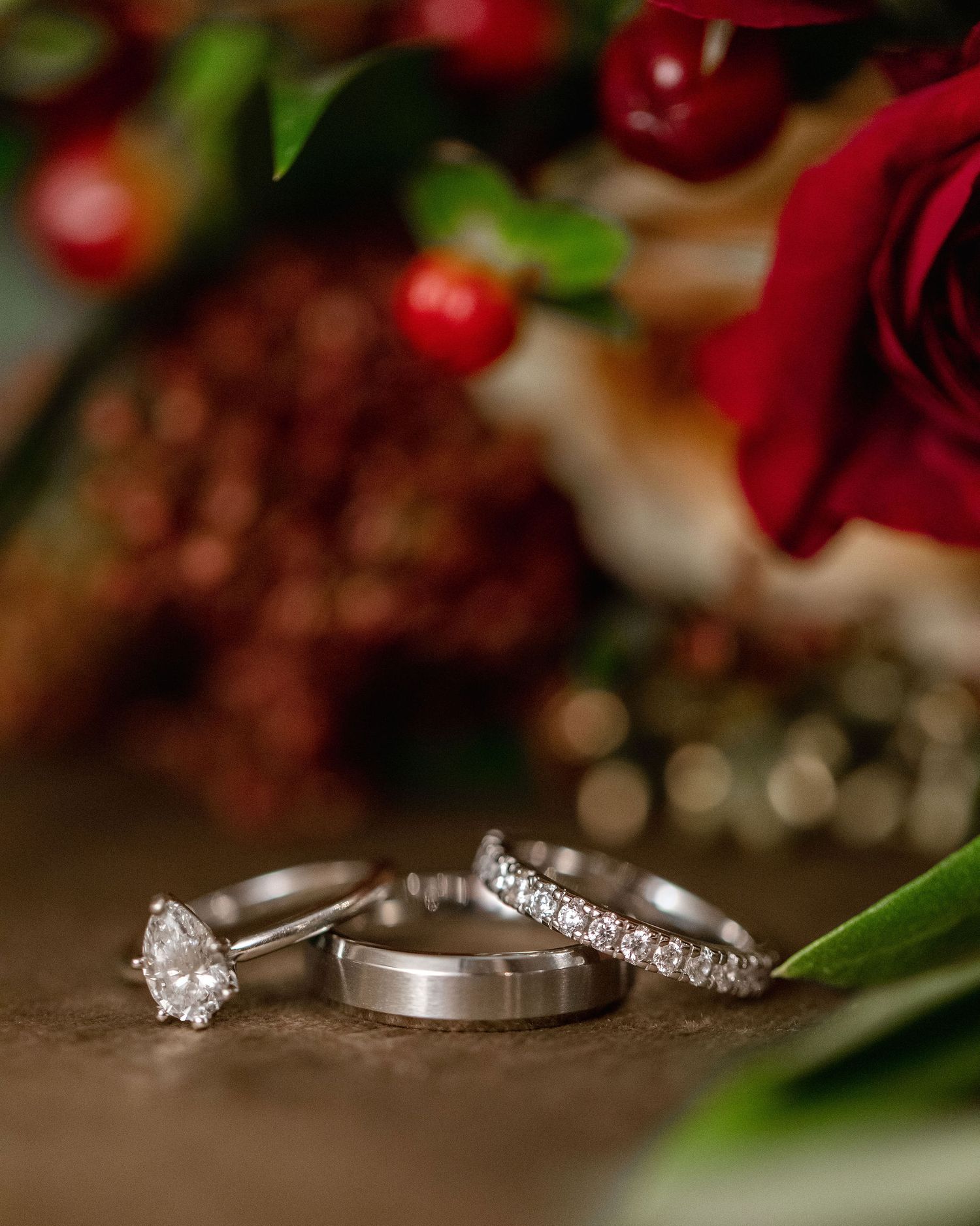 Wedding rings photographed with red roses and cherries in romantic lighting.
