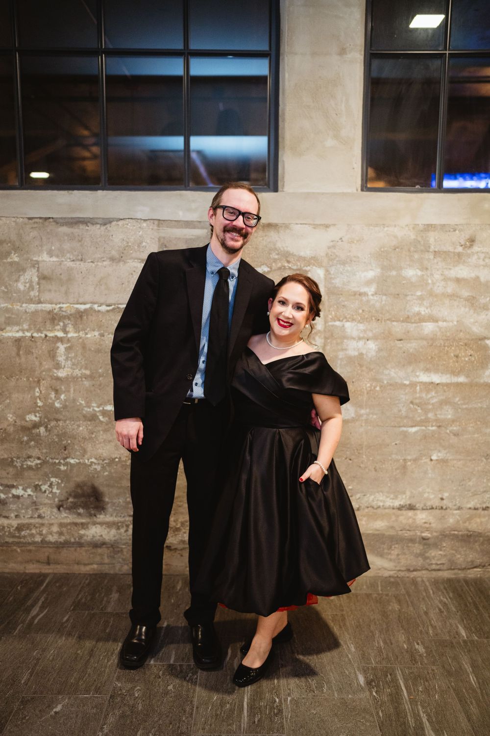Couple in formal attire against industrial concrete wall.