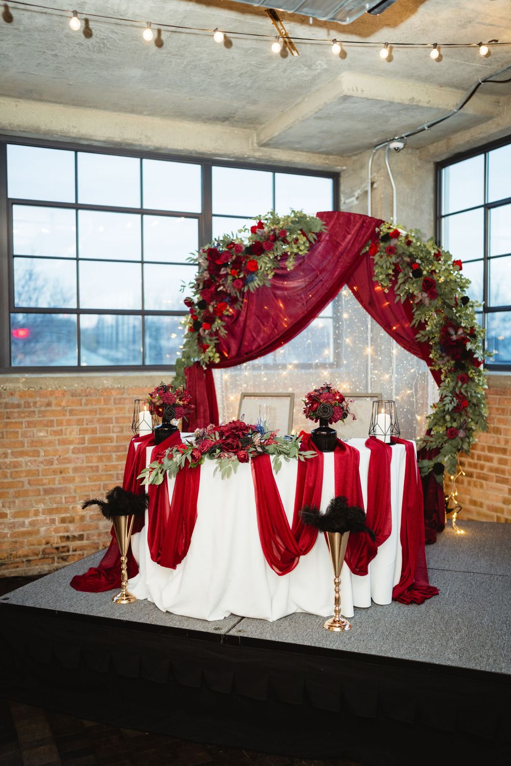 Wedding arch decorated with red draping and roses against industrial windows.