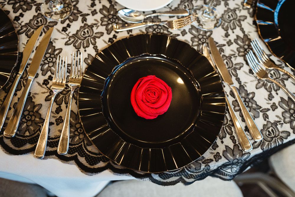 Black charger plate with red rose centerpiece and metallic place settings.