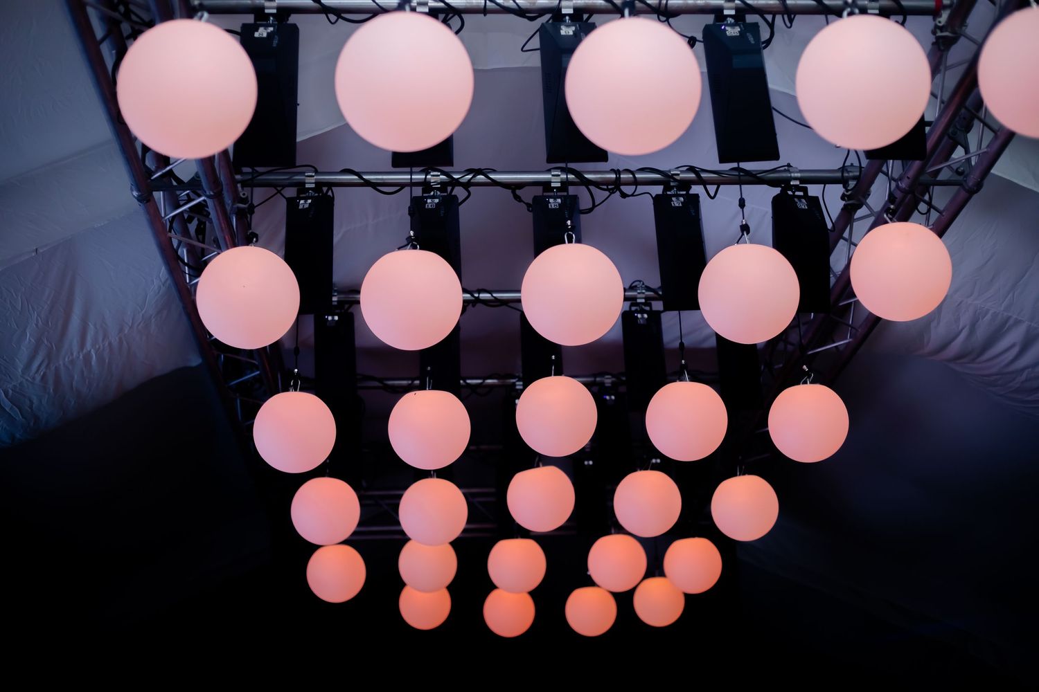 Grid of glowing pink spherical lights on black truss framework at event venue.