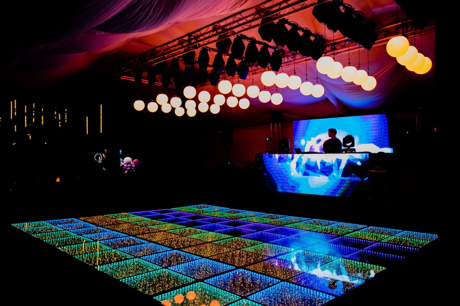 Empty LED dance floor with globe pendant lights and DJ booth at elegant indoor event.