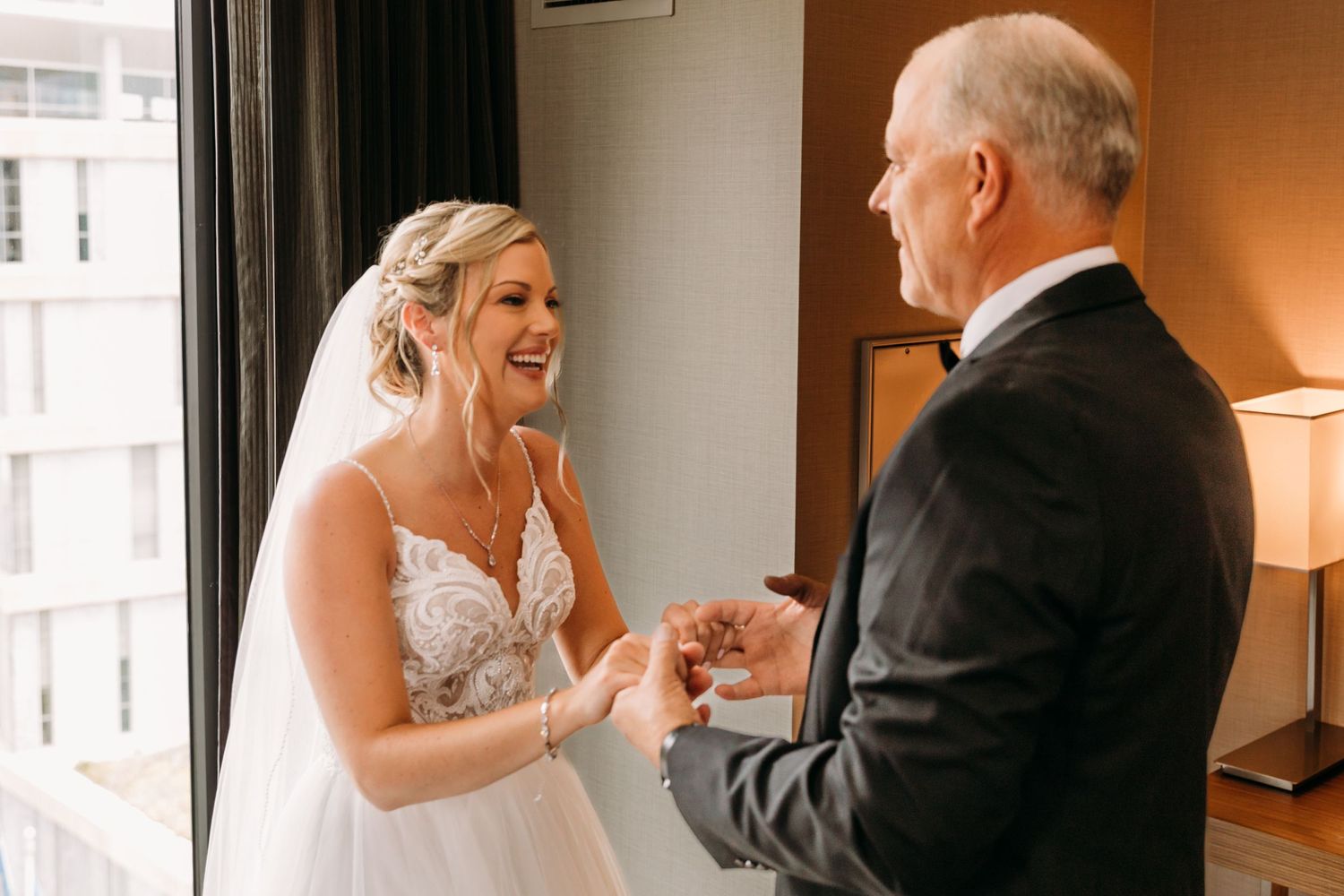 A tender moment between a bride in a lace gown and an older gentleman in a formal room.