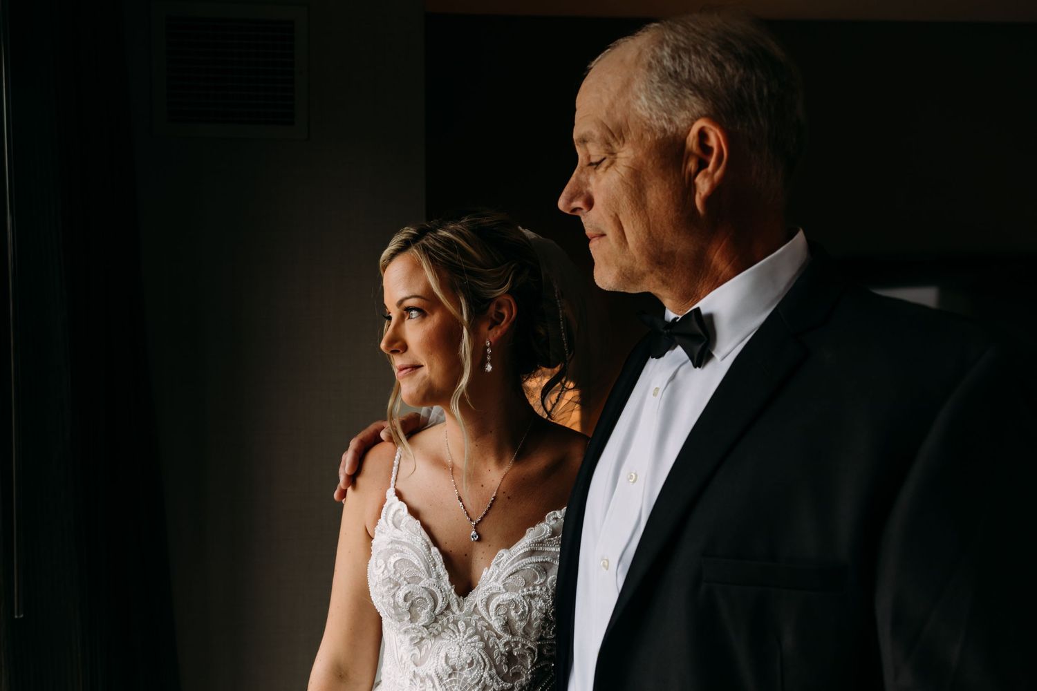 A dramatic side-lit portrait in a dimly lit room during wedding preparations.