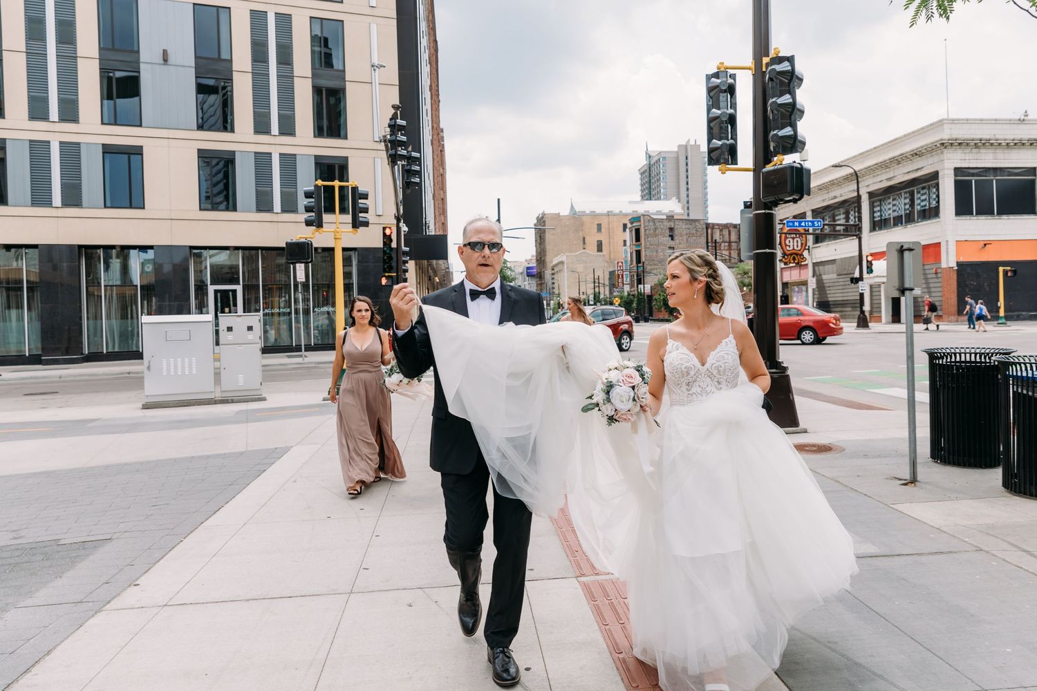 A couple walking down a city street, with the bride holding up her white wedding dress.