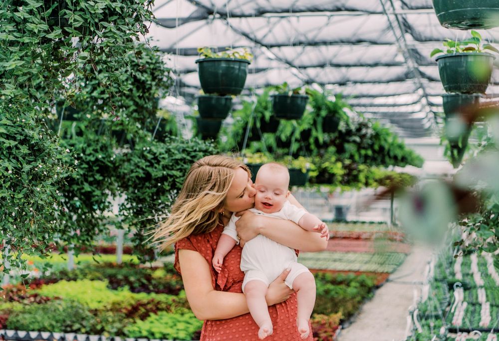 Inside a garden nursery greenhouse with hanging planters, lush greenery and plants surrounding a moment shared between two people.