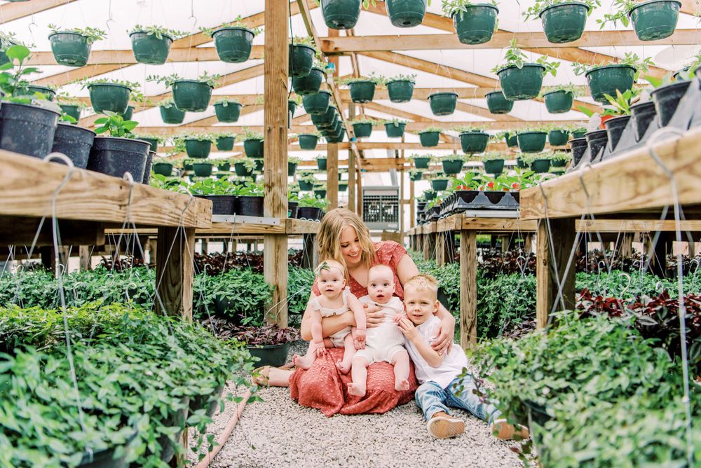 People sitting in a greenhouse surrounded by hanging green plants and pots at a garden nursery.