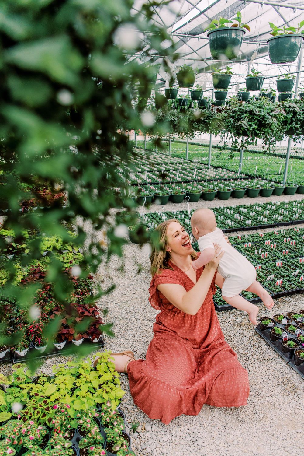 A joyful scene in a greenhouse nursery with rows of plants and hanging baskets overhead.