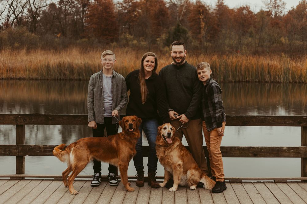 Family and their dogs posing on a wooden dock by a lake during autumn.
