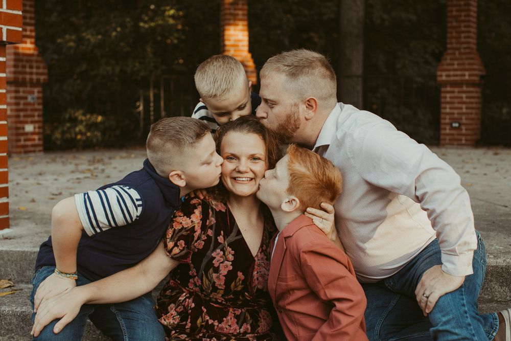 A joyful family moment captured outdoors against a brick backdrop in warm evening light.