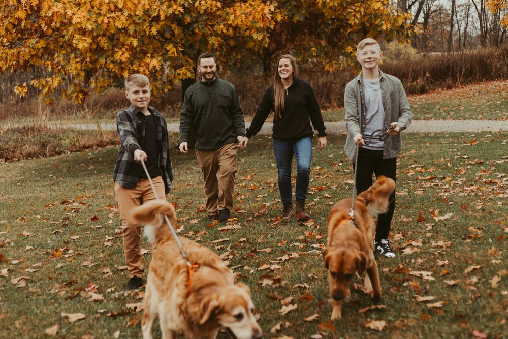 Group photo with golden retrievers in a park setting during fall season.