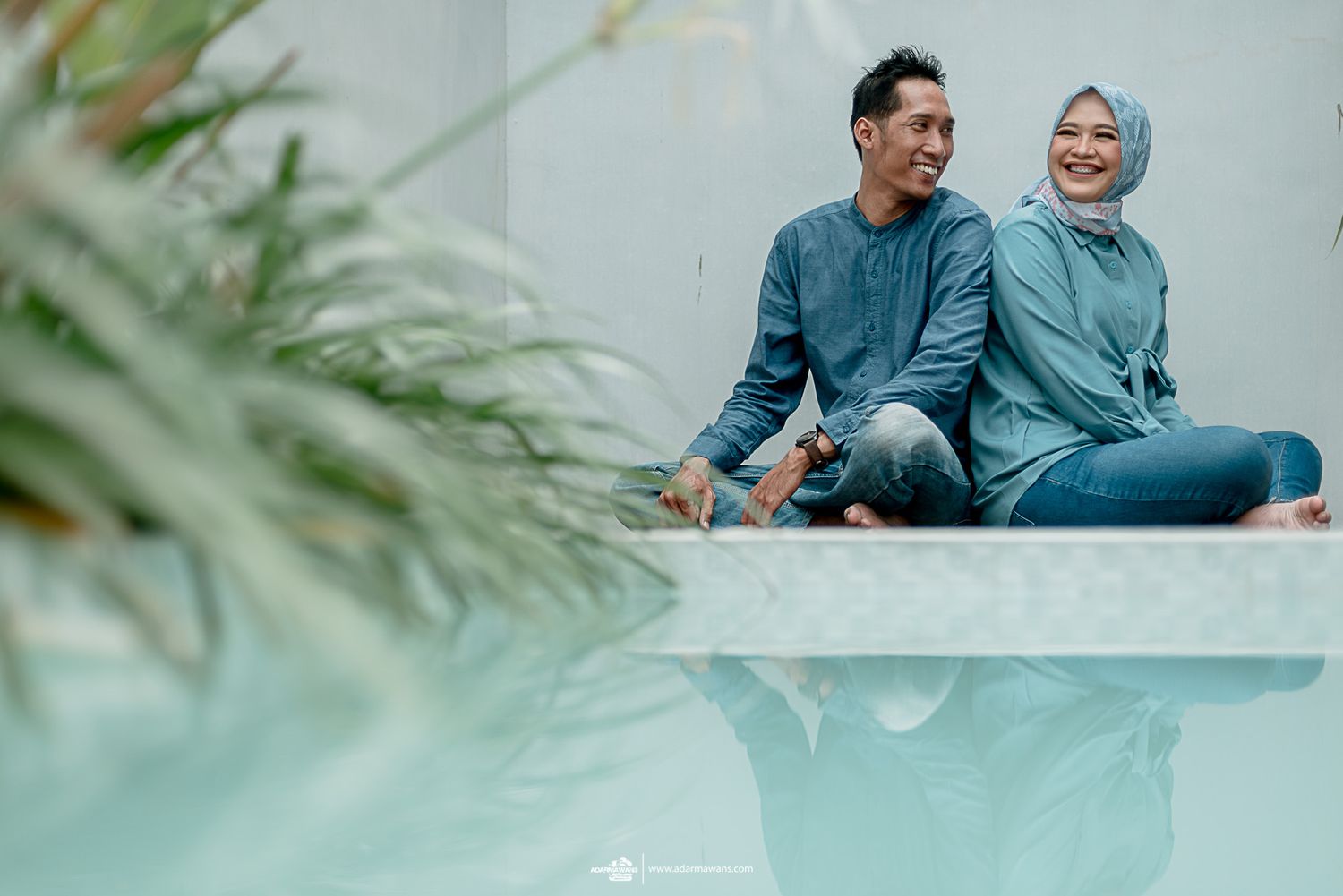 Couple in coordinating blue outfits share a casual moment on an outdoor ledge.