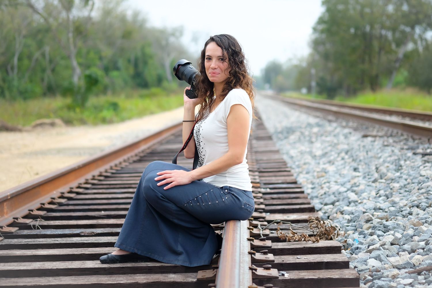 Professional photographer poses with camera on train tracks during golden hour.