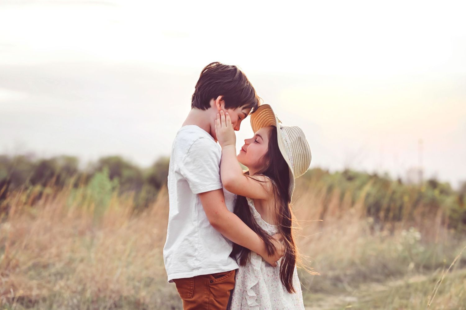 A young romantic couple sharing an intimate moment in a golden field at sunset.