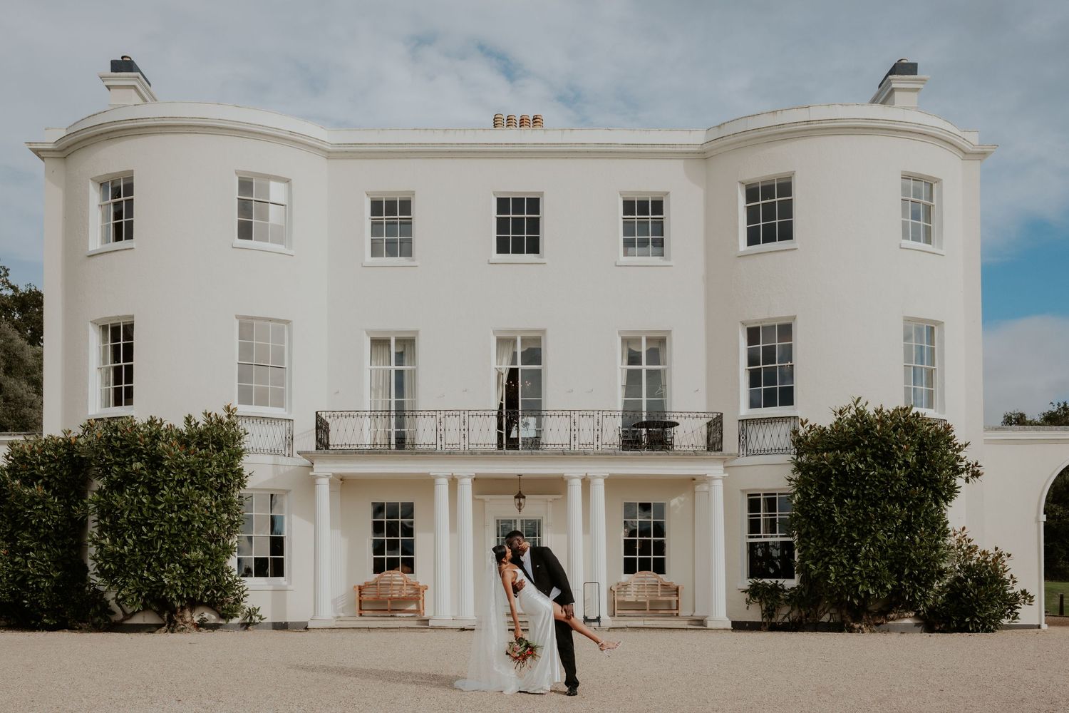 Elegant white Georgian mansion serves as backdrop for wedding portrait.