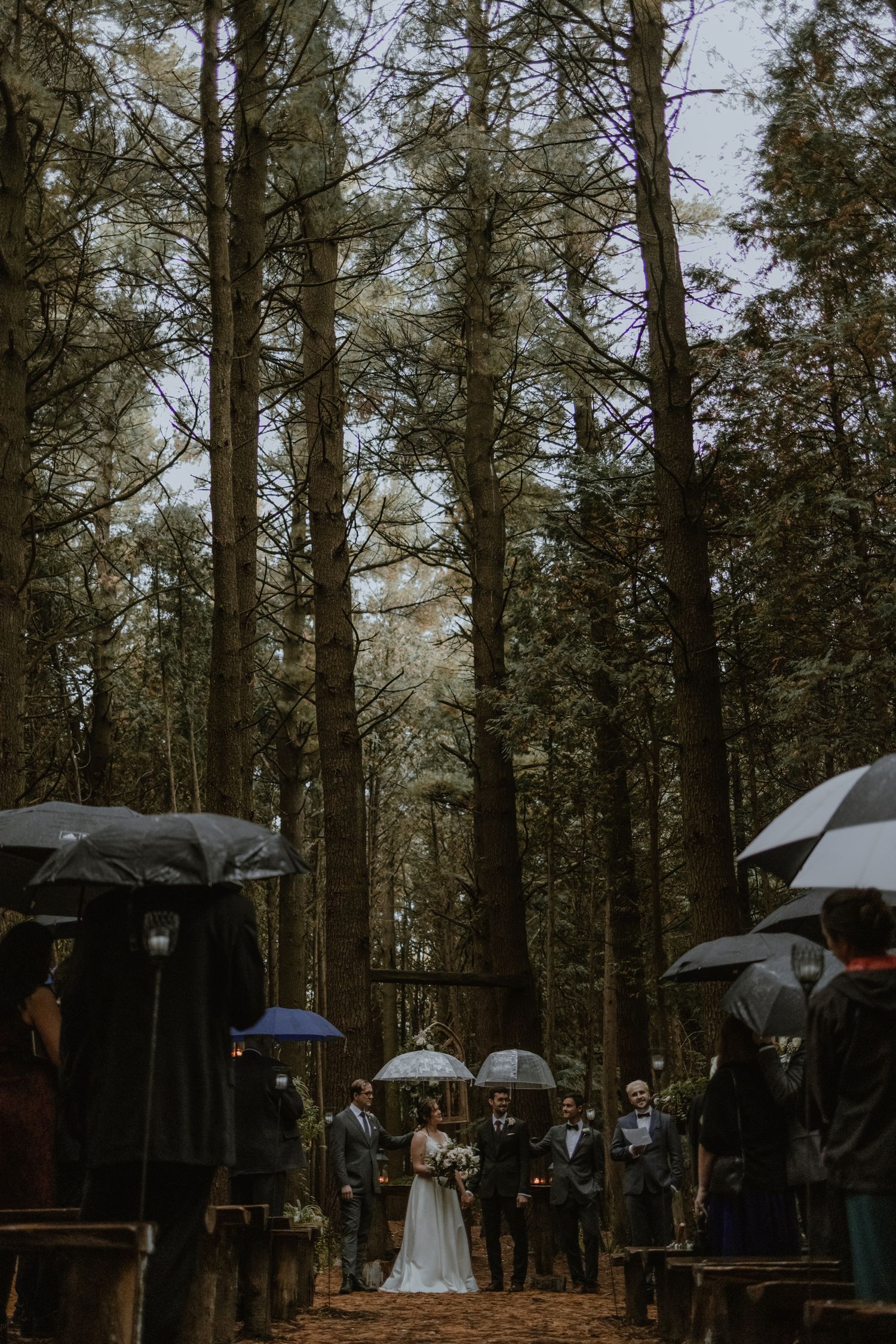 a wedding ceremony with guests looking on under umbrellas during a rainy outdoor wedding at Whispering Springs