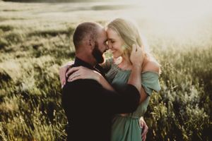 A romantic couple embraces in a sunlit field of tall grass during golden hour at sunset.