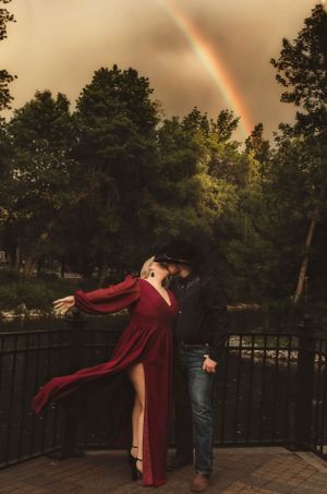 A romantic moment on a bridge with a stunning rainbow in the background.