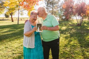 An elderly couple sharing a tender moment in a park with autumn trees.