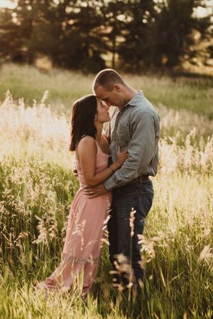 A romantic couple embraces in a sunlit meadow of tall grass during golden hour at sunset.