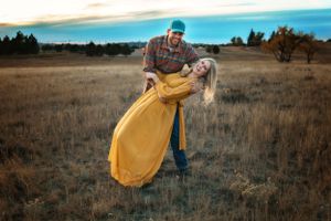 A playful couple in a golden field at sunset with dramatic lighting.
