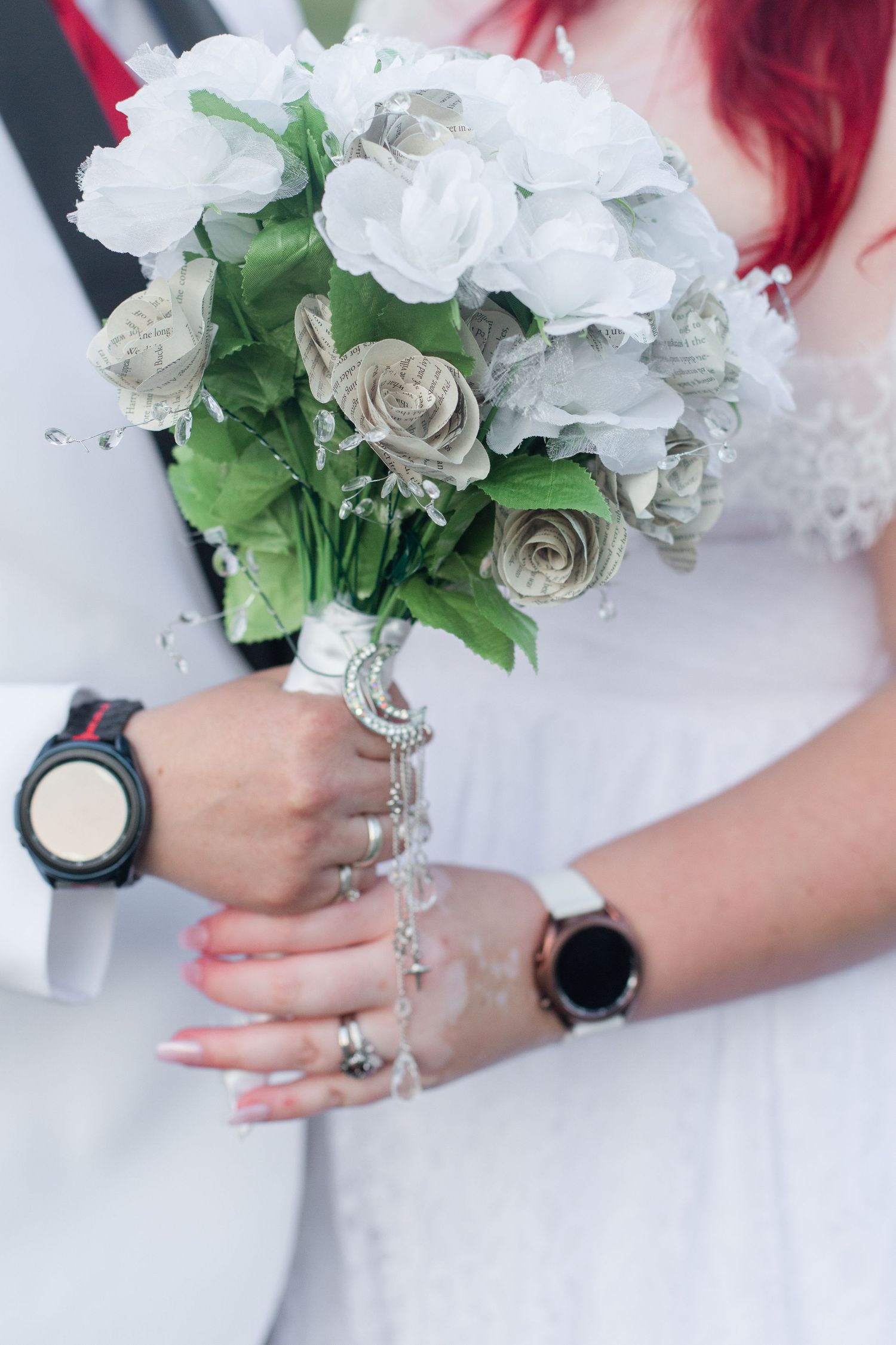Close-up of bridal bouquet with white and silver roses held by hands adorned with rings.