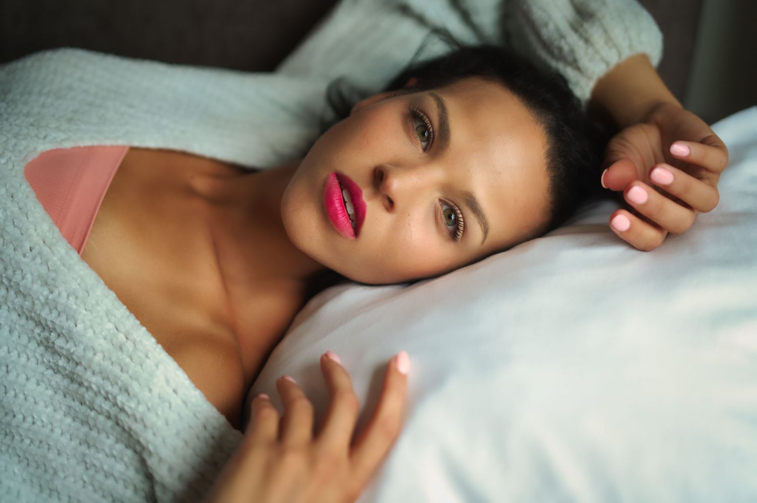 Soft natural light portrait with bold red lipstick on white bedding.