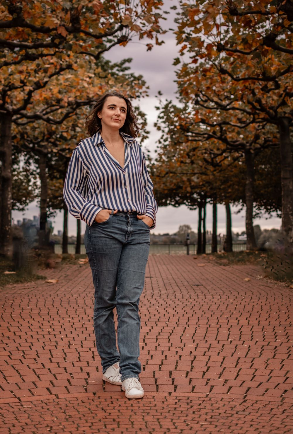 Autumn portrait on brick path with striped shirt and jeans among orange trees.