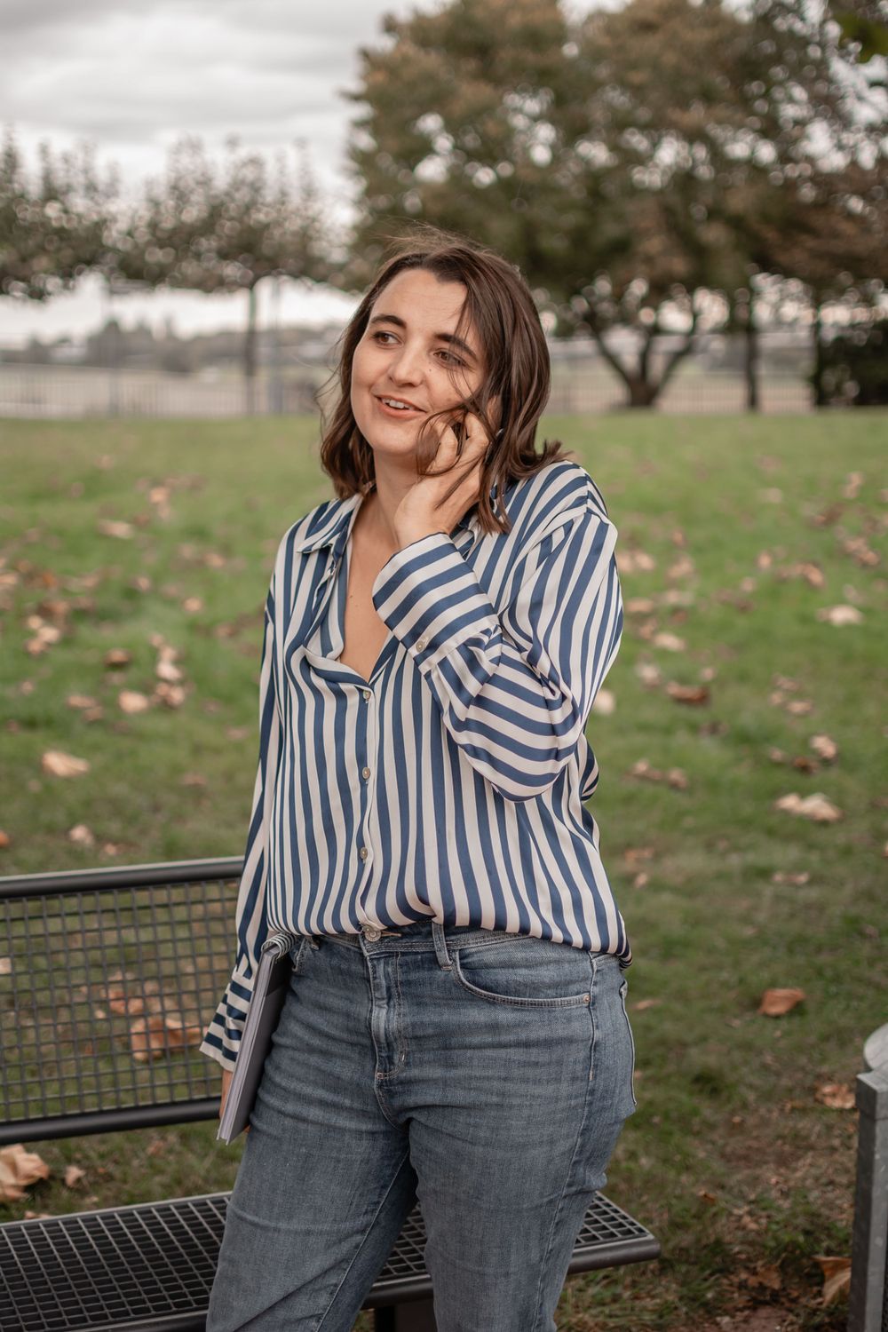 Casual outdoor portrait with striped button-down shirt and jeans in park setting.