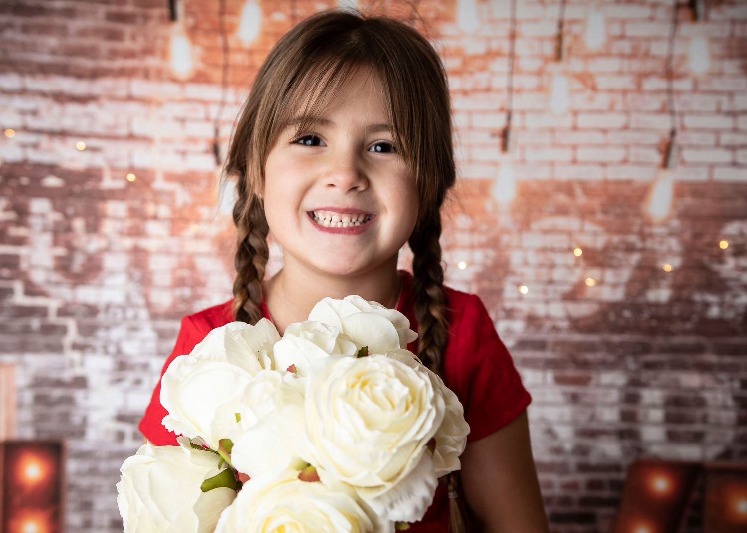 A person in red holds a beautiful bouquet of white roses against a rustic brick wall backdrop.