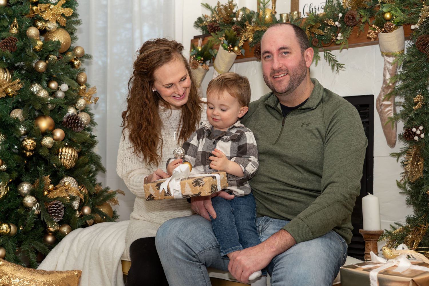 Family unwraps Christmas presents together near decorated tree and fireplace.