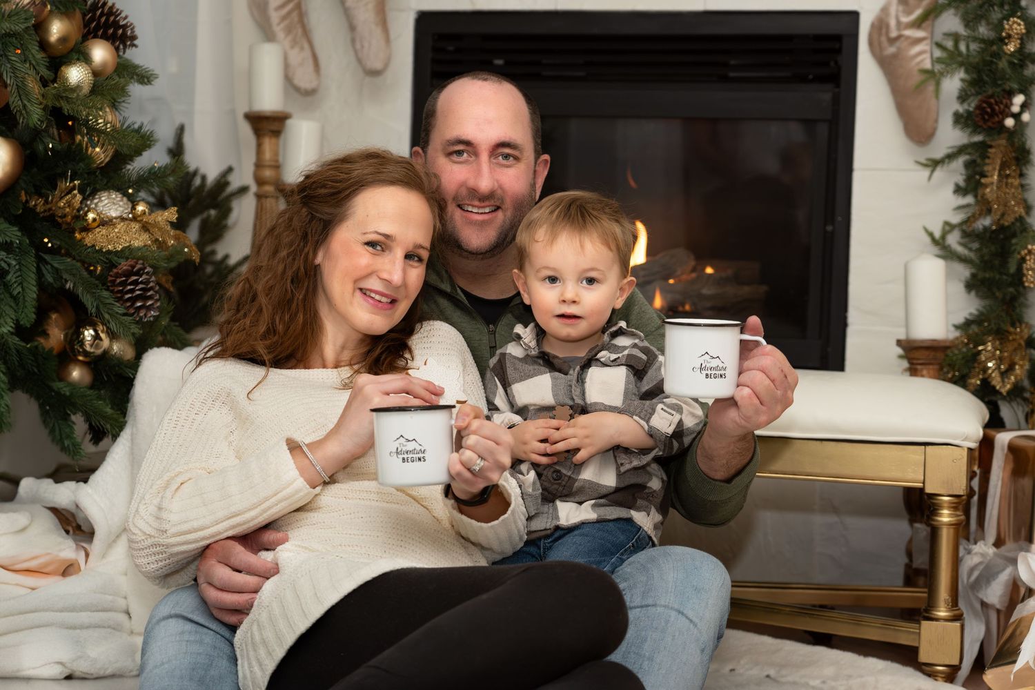 Family sits together holding coffee mugs by decorated Christmas fireplace.