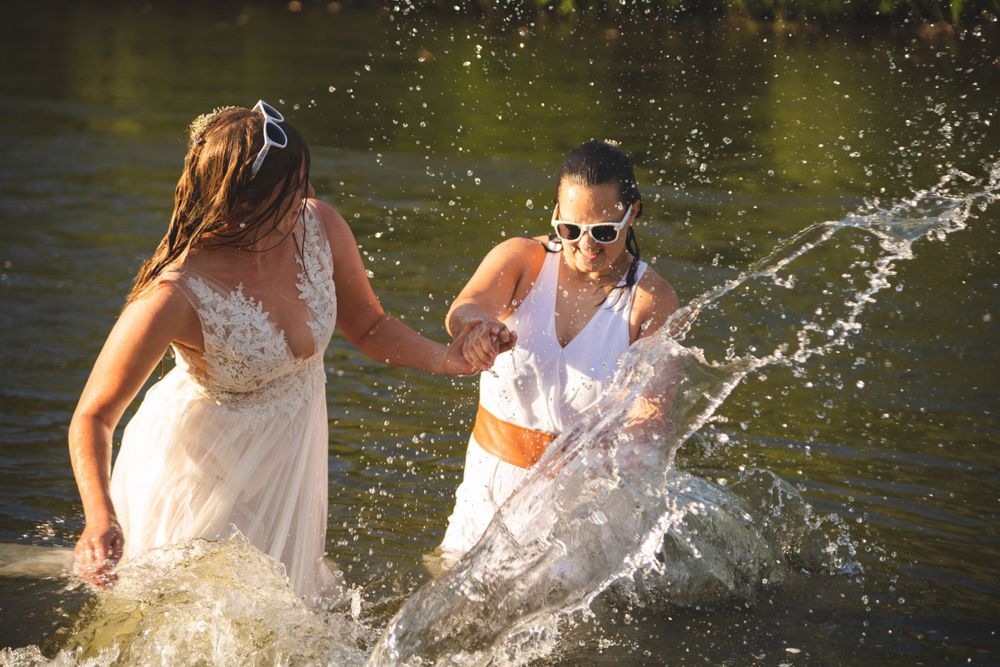 same sex female couple splashing in their wedding dresses in a river