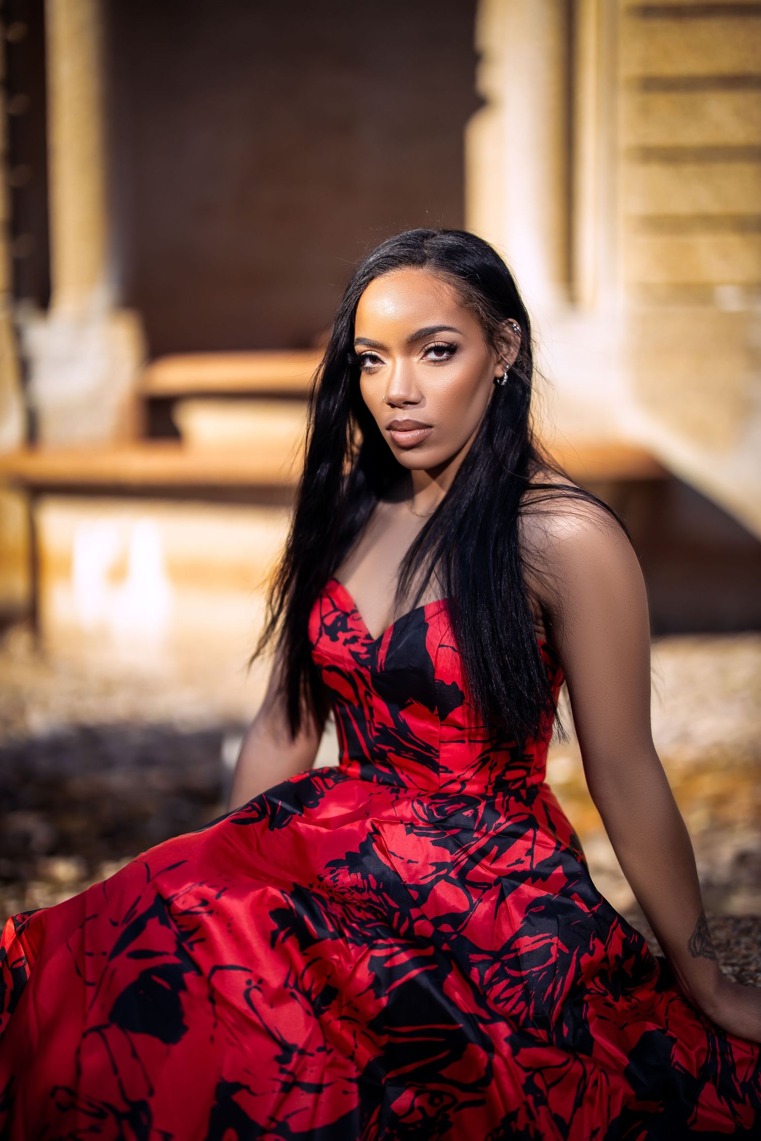 A person in a red and black patterned gown poses against golden stone architecture.