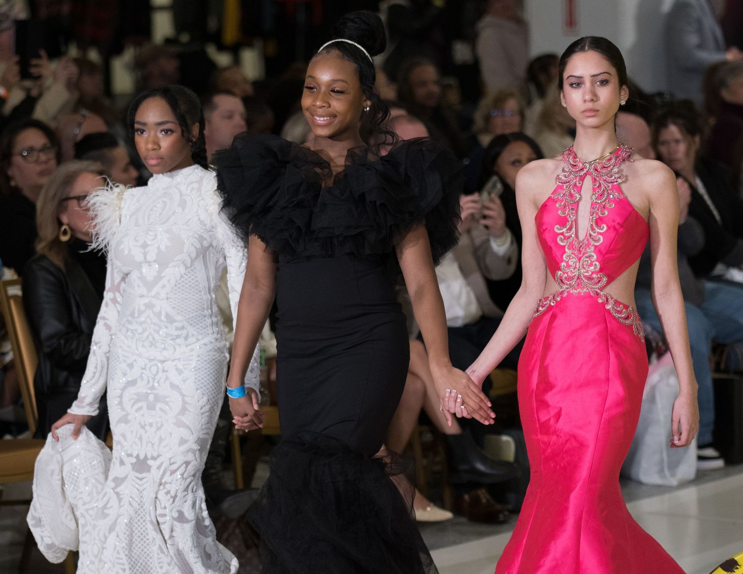 Three models showcase elegant evening gowns in white, black and hot pink on the runway.