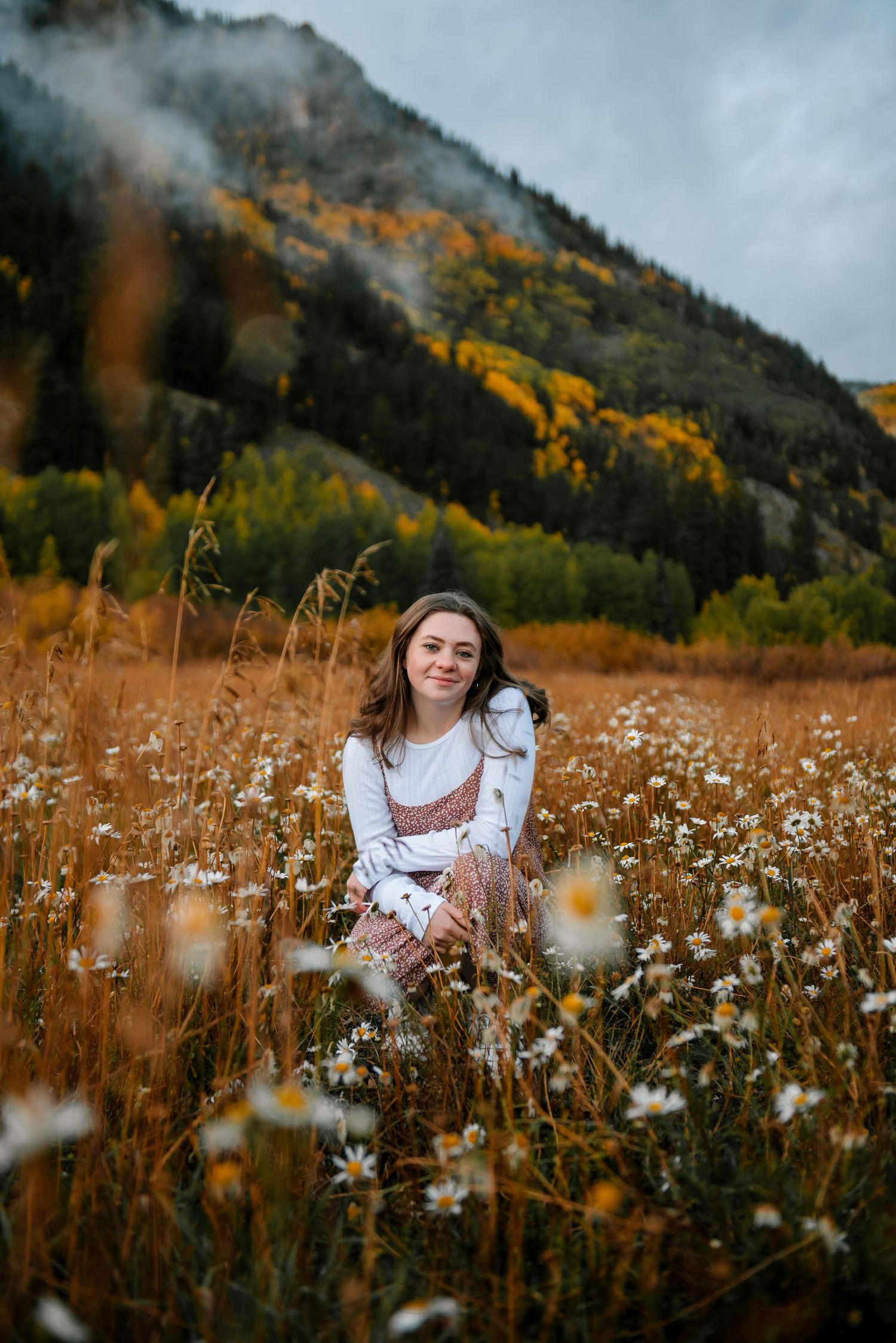 Portrait in a wildflower meadow with misty mountains and fall foliage.