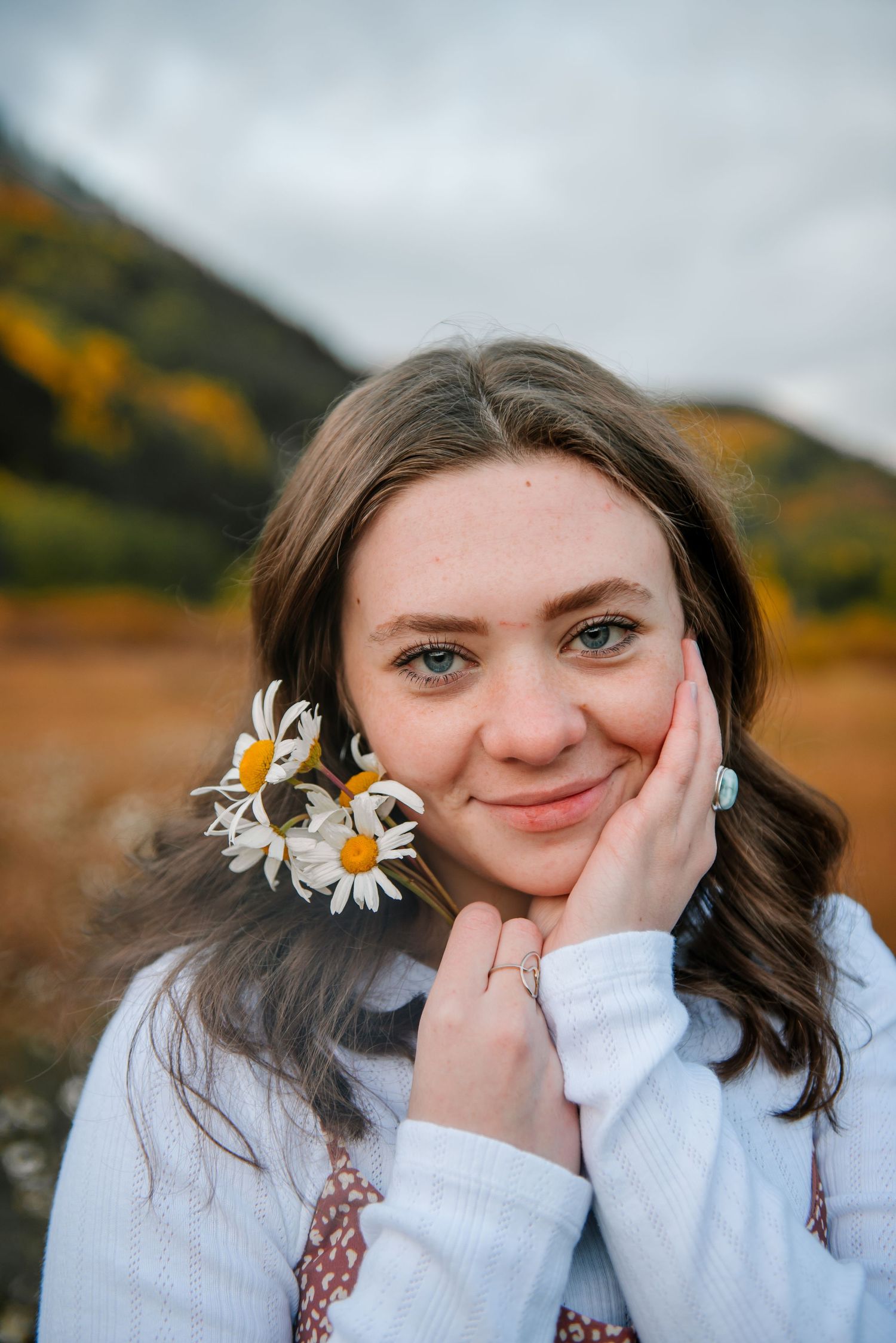 Portrait with daisy flowers against autumn mountain landscape.
