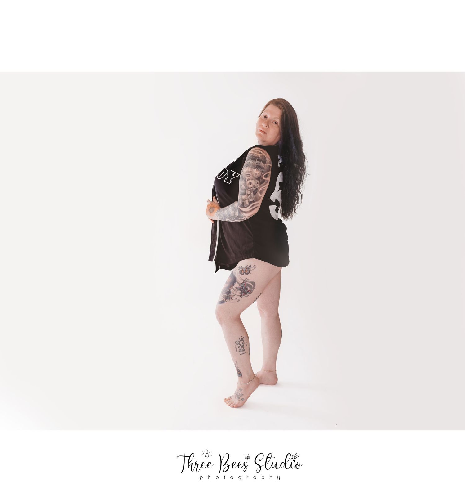 Artistic portrait of a person in a black dress showing off tattoos against a white background.