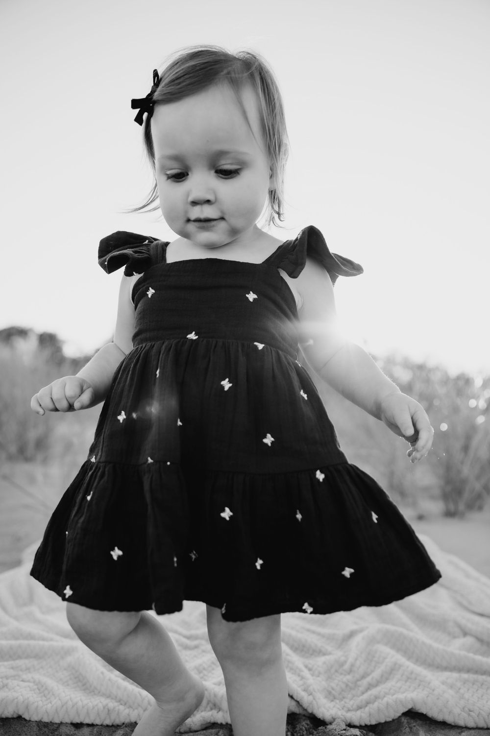 Black and white portrait of a twirling toddler in a polka dot dress on a blanket. third beach middletown rhode island