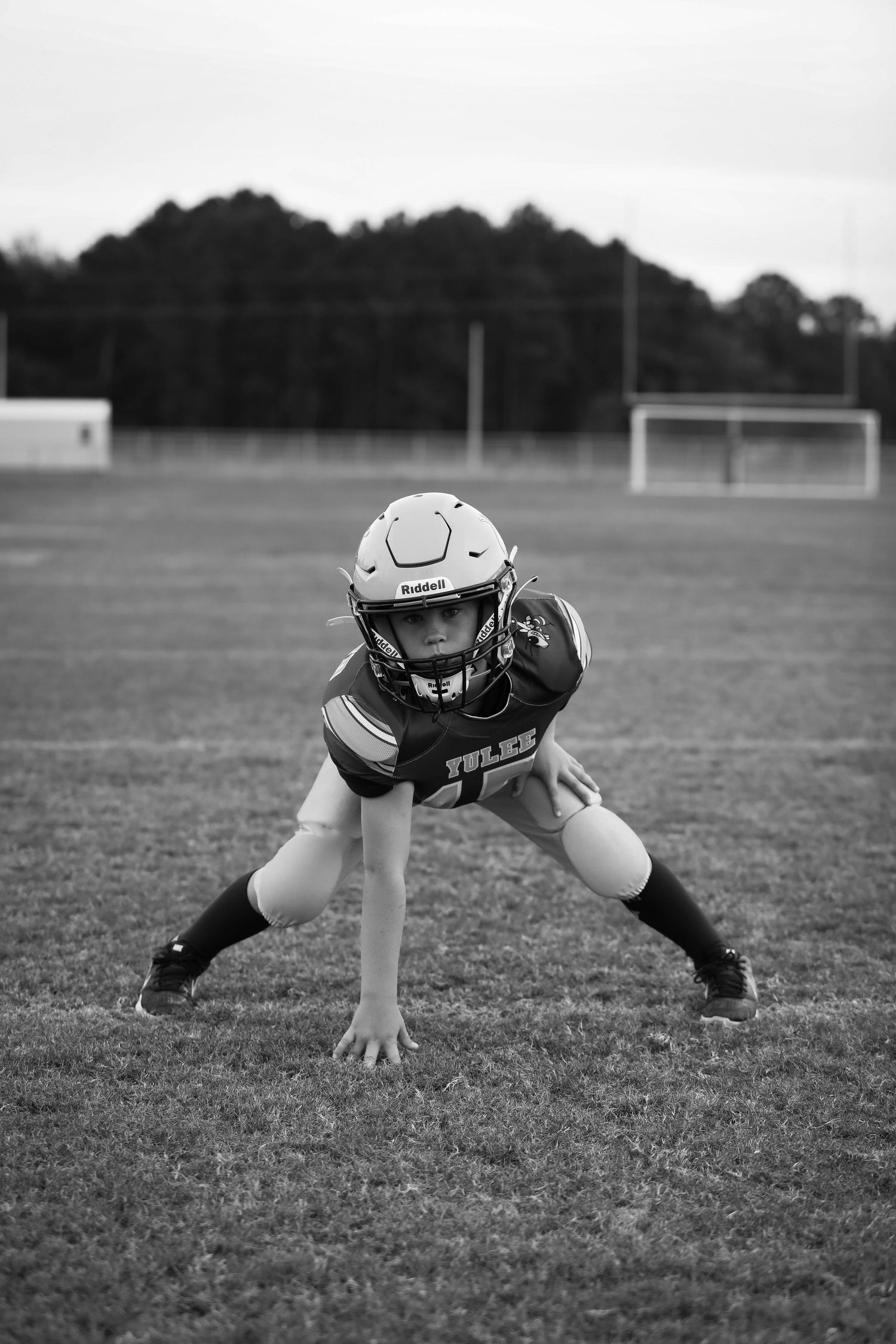 Football player in protective gear crouches in ready position on field.