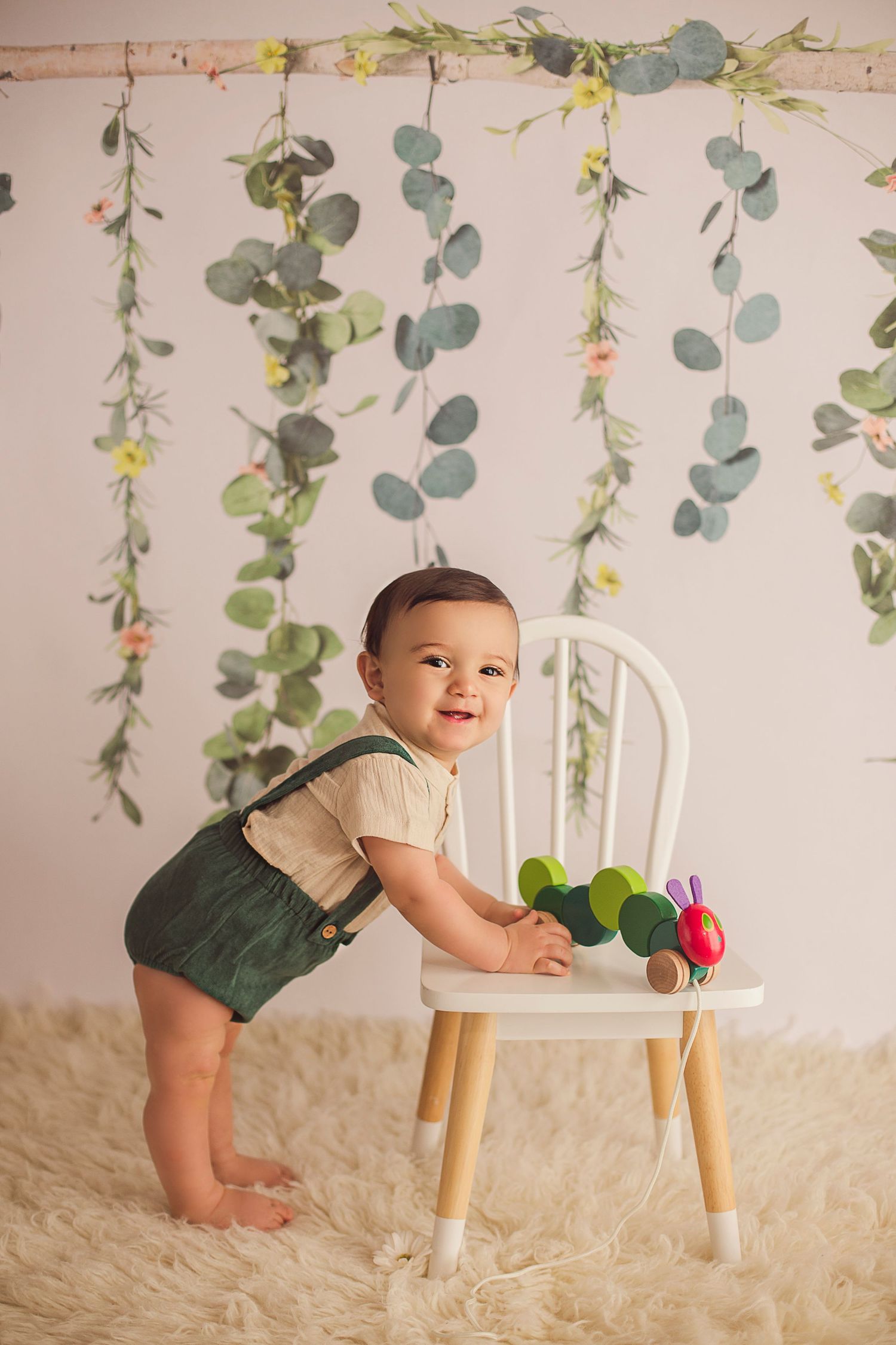 baby standing up holding on to a chair greenery backdrop
